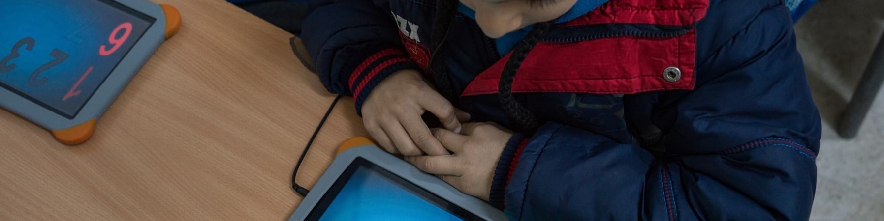 bambino seduto al banco studia con un tablet davanti
