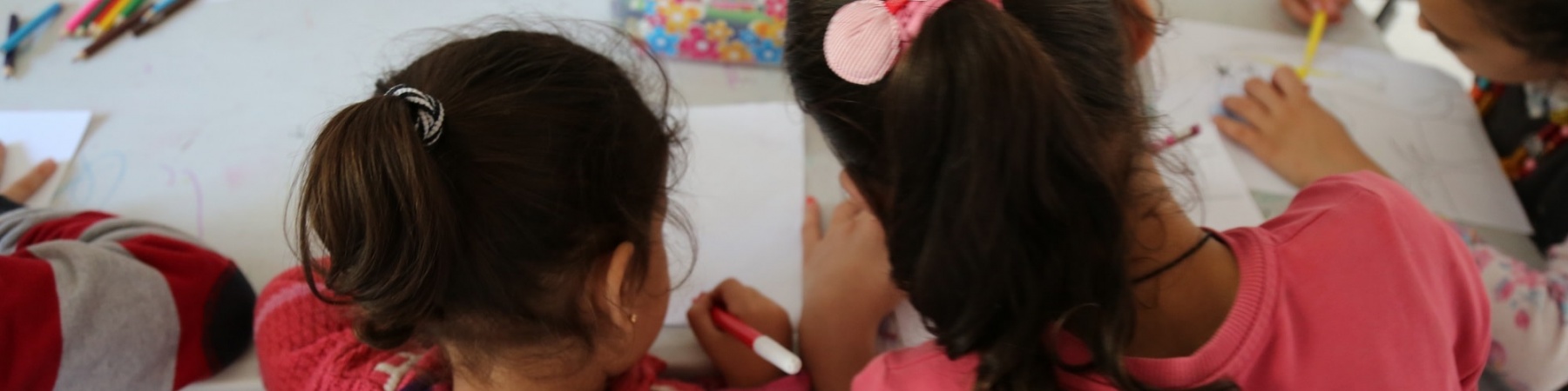 due bambine di spalle al banco di scuola che disegnano