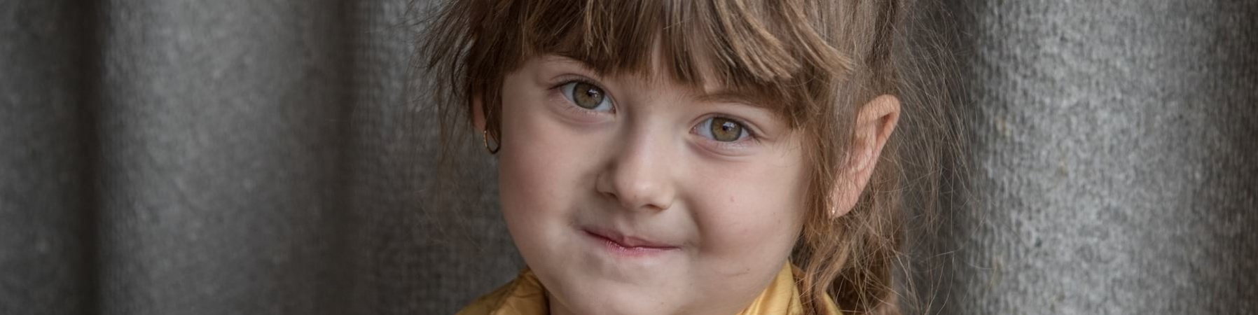 primo piano di bambina sorridente bionda con la coda sorridente. Indossa una giacca gialla e una maglietta celeste