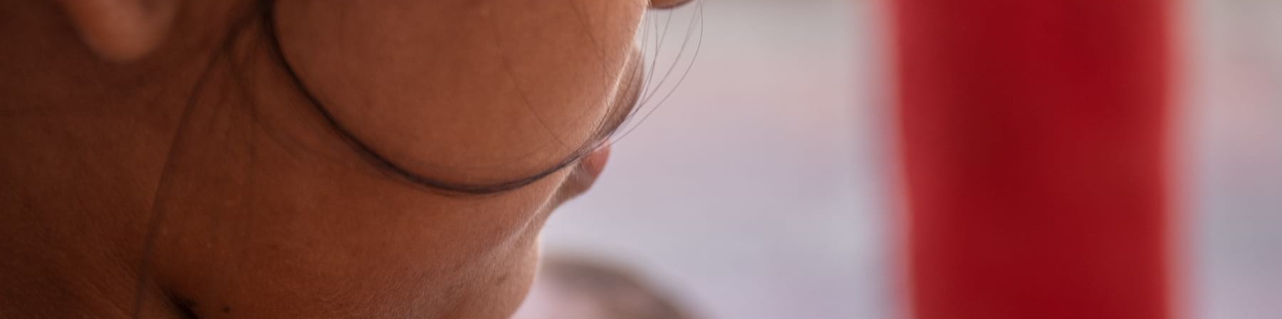 Inquadratura di una parte del volto di una donna, focalizzato sulla guancia per non farla riconoscere. Sullo sfondo il viso di un neonato