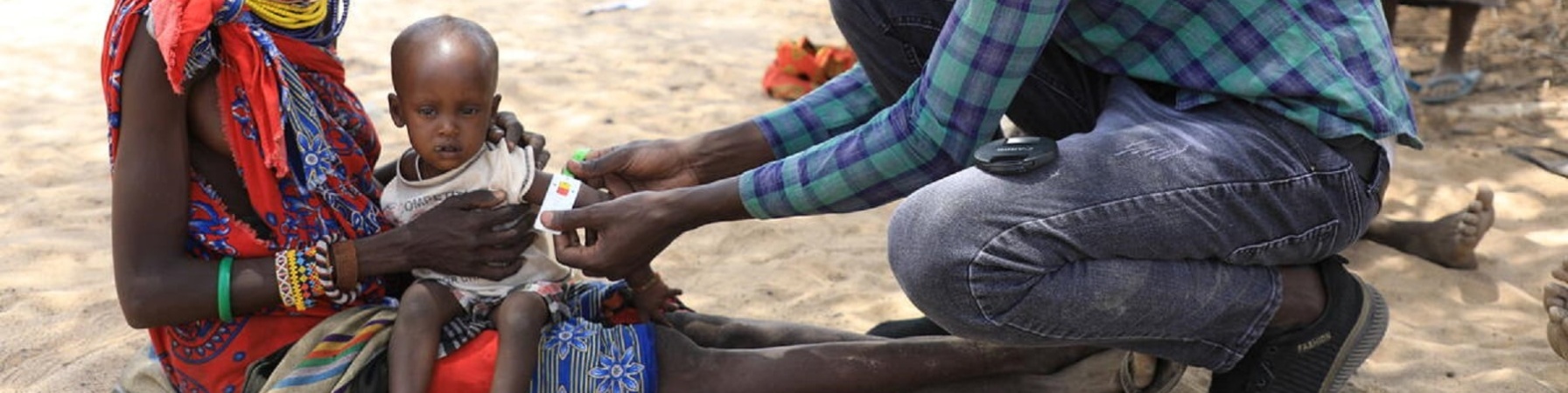 Bambino keniota in braccio alla madre mentre un dottore misura il livello di malnutrizione mettendo il braccialetto MUAC attorno al braccio 