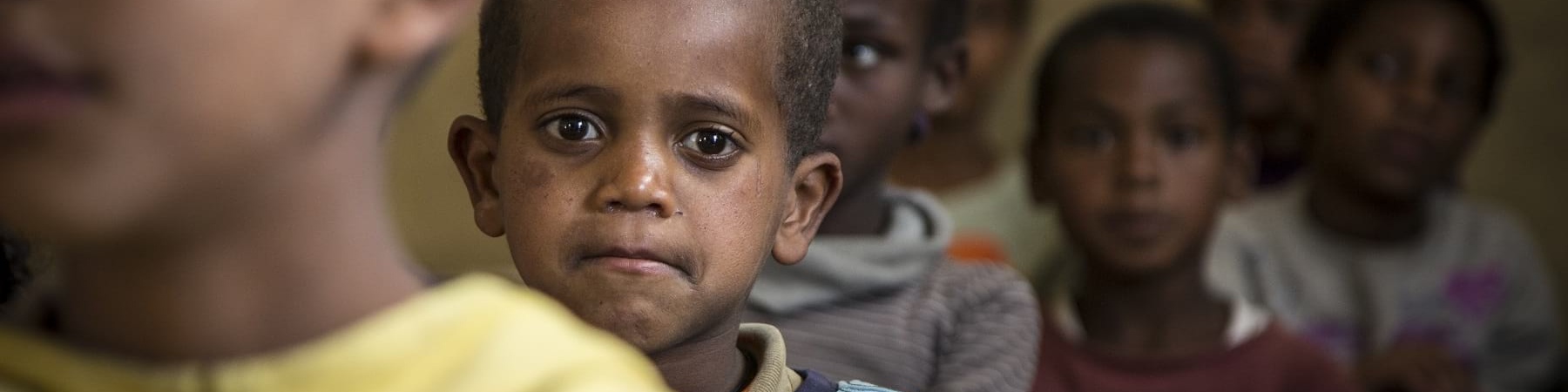 Primo piano di un bambino etiope con maglietta azzura che compare dietro al viso di un altor bambino davanti a lui che si vede sfocato