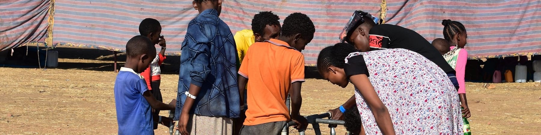 un gruppo di bambini e ragazzi etiopi in un campo per rifugiati si affollano intorno a una fonte d'acqua per raccoglierla con le taniche