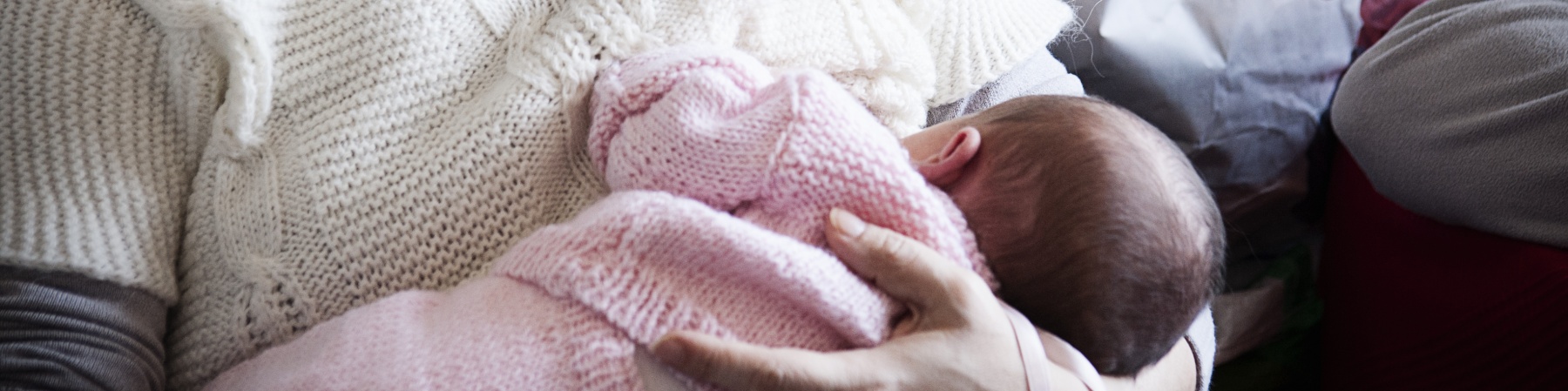 donna-maglione-bianco-tiene-in-braccio-neonato-tutina-rosa