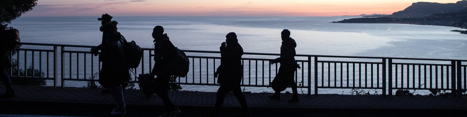 Quattro sagome in controluce affacciate da una ringhiera sul mare al tramonto