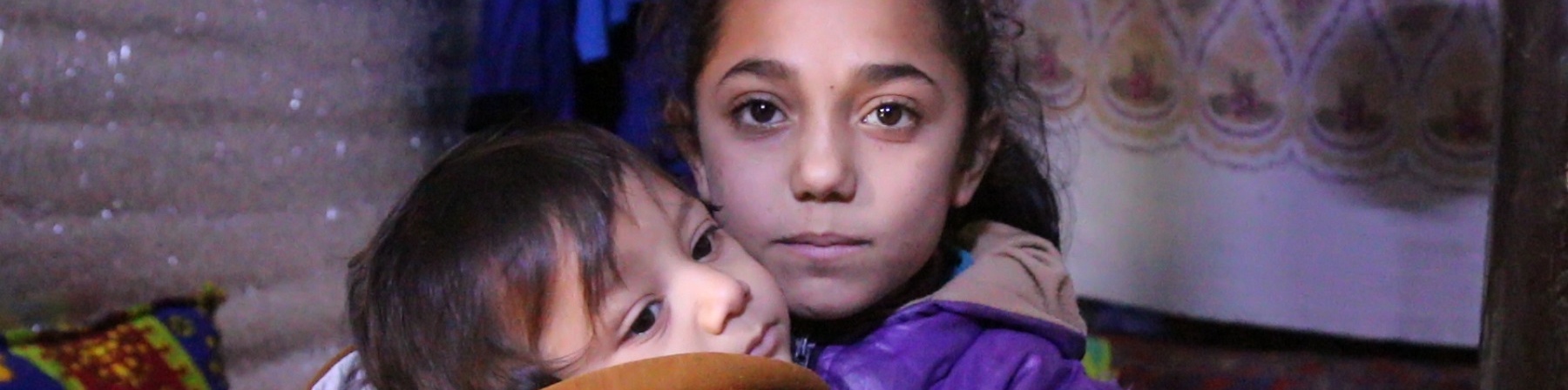 Freddo Siria bambina con cappotto viola tiene in braccio un bambino