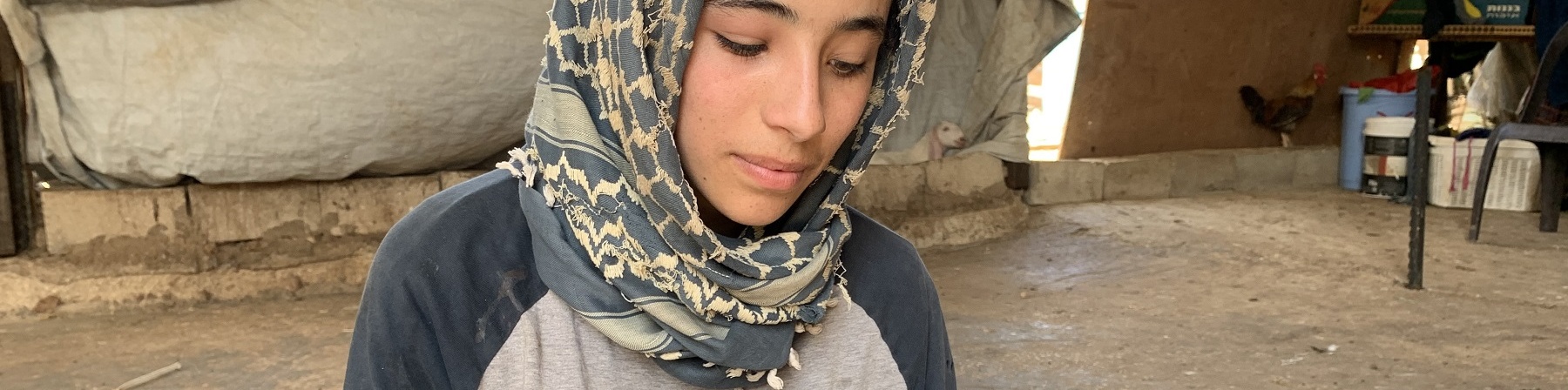 Ragazza palestinese con kufia in testa è seduta a terra e legge un quaderno che tiene poggiato sulle ginocchia