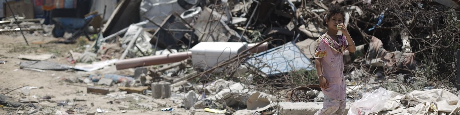 bambina palestinese cammina davanti a un cumulo di spazzatura.