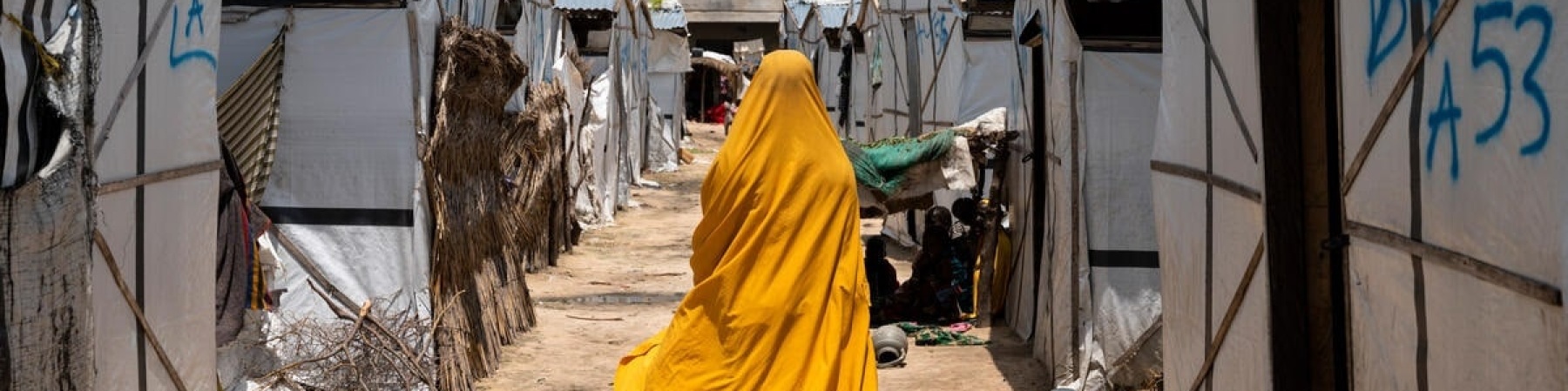 ragazza con vestito e velo giallo che attraversa un'area del camp profughi
