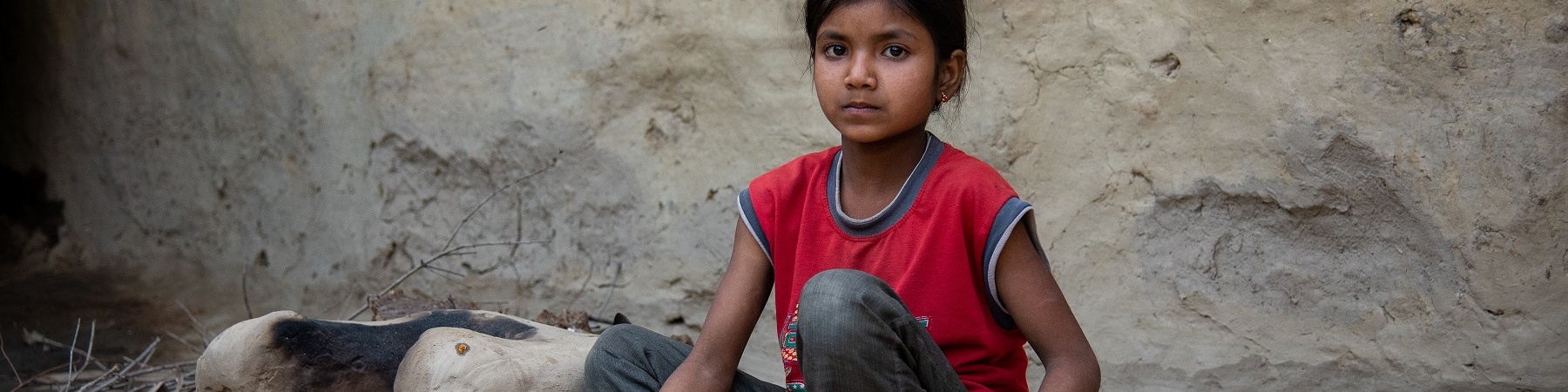 Bambina indiana seduta a terra tiene in mano un contenitore in corda con dentro il riso