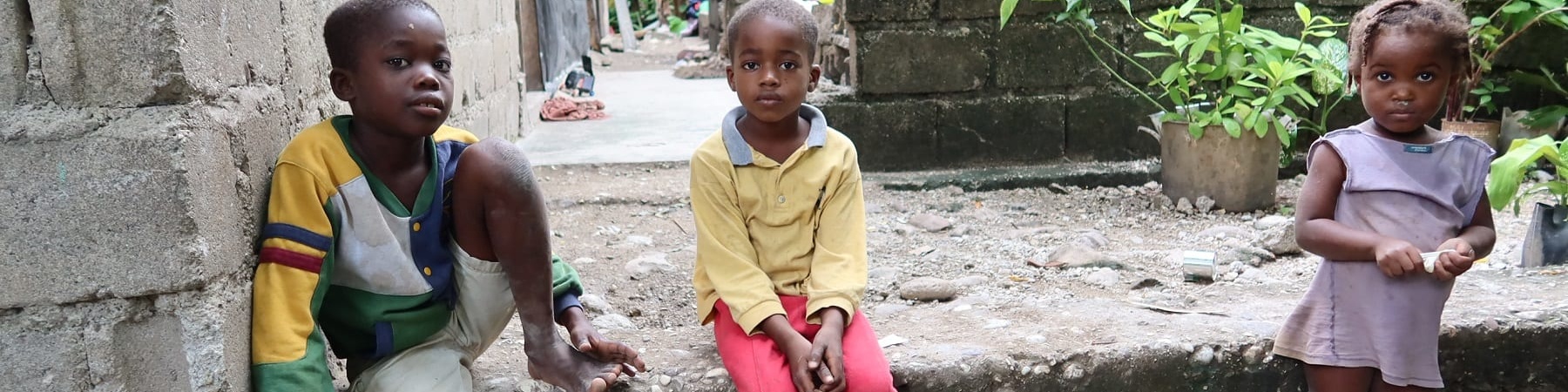 Tre bambini haitiani seduti su un gradino guardano in camera