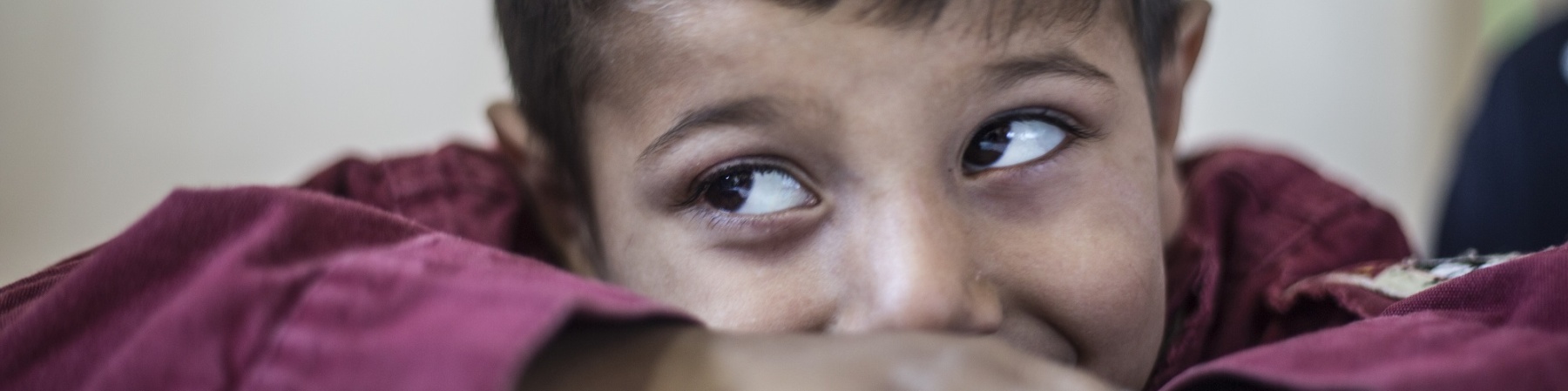 Bambino al tavolo, primo piano, alza gli occhi a sinistra sorridendo