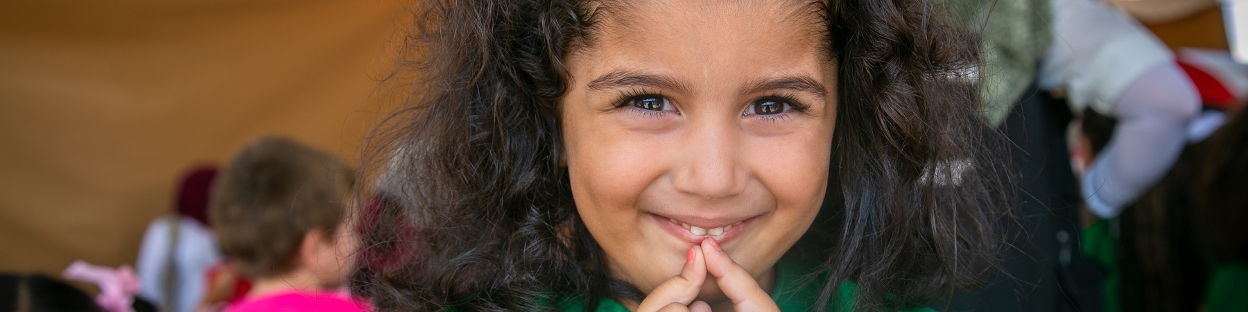 Foto mezzo busto bambina riccia con fiocco azzurro in testa e con le mani giunte davanti alla bocca