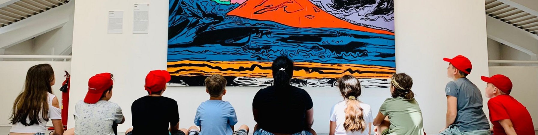 studenti e studentesse seduti a terra mentre guardano un quadro di un vulcano