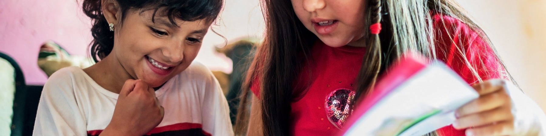 due bambine leggono insieme un libro. Una con i capelli castano scuro raccolti e l'altra con i capelli castano chiaro sciolti.