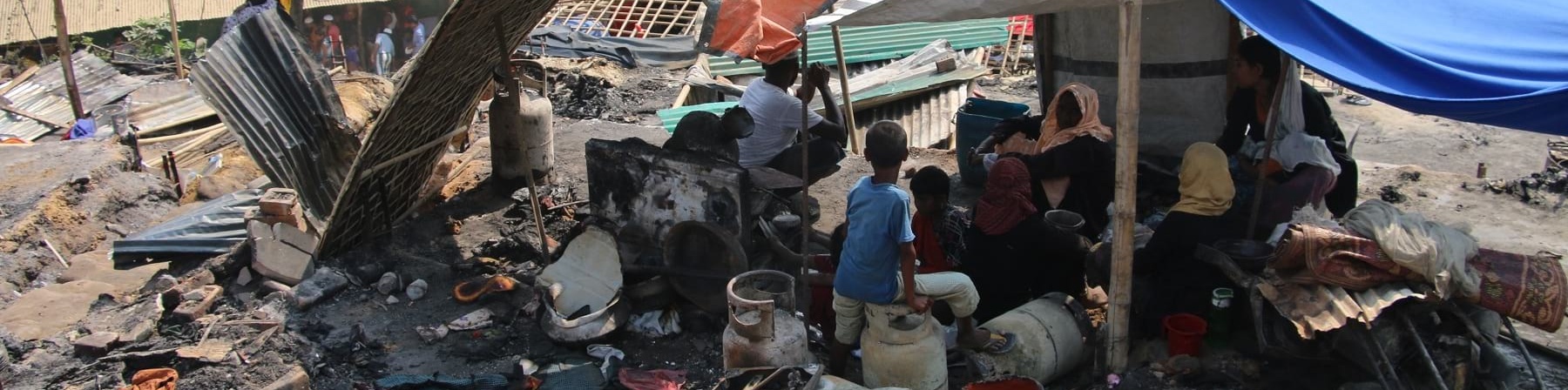 Tenda di fortuna nel mezzo di cenere e resti incendiati nel campo di coxs bazar in bangladesh. Sotto la tenda si ripara una famiglia Rohingya di varie persone 