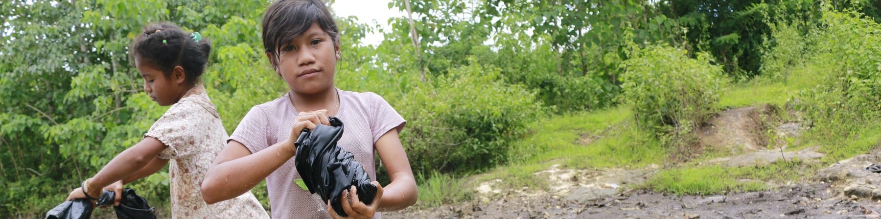 Due bambine indonesiane in piedi in un torrente strizzano i panni