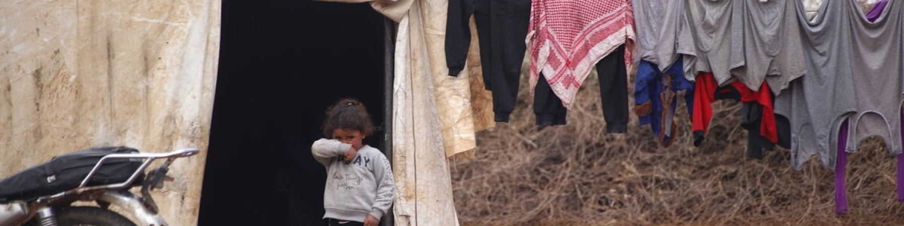 bambina che si copre il viso di fronte alla sua tenta dopo le inondazioni in Siria