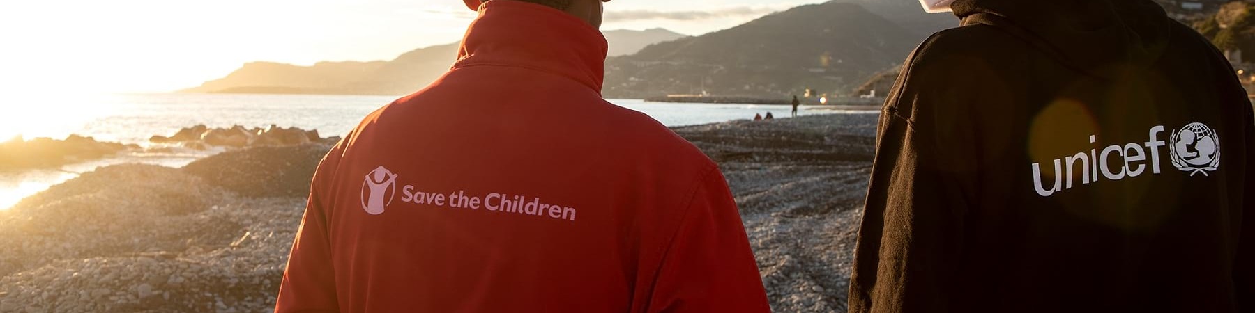 Due operatori, uno save the children e l altro Unicef, di spalle guardano un tramonto davanti a loro.