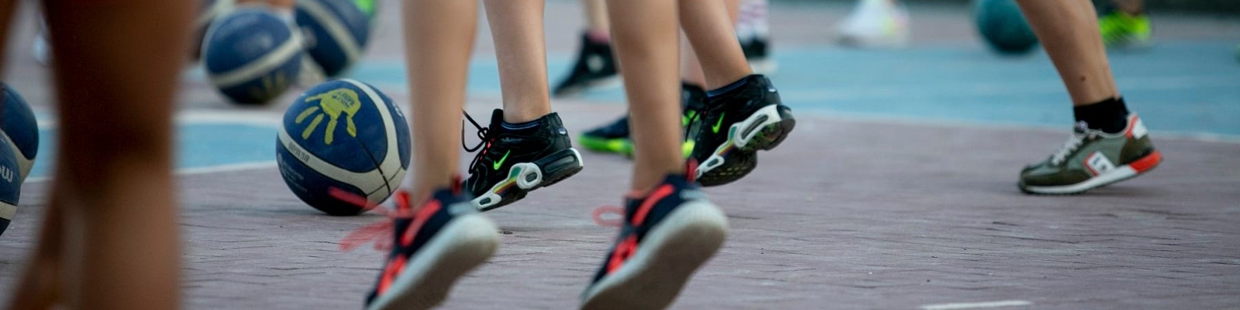 Primo piano di gambe di bambini e bambine che giocano con la palla in un campo da basket