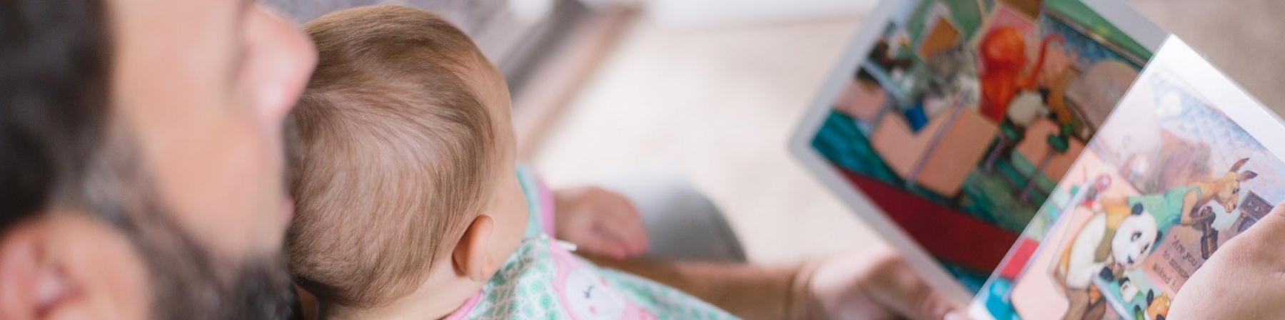 bimba neonata in braccio al papà mentre leggono insieme un libro illustrato