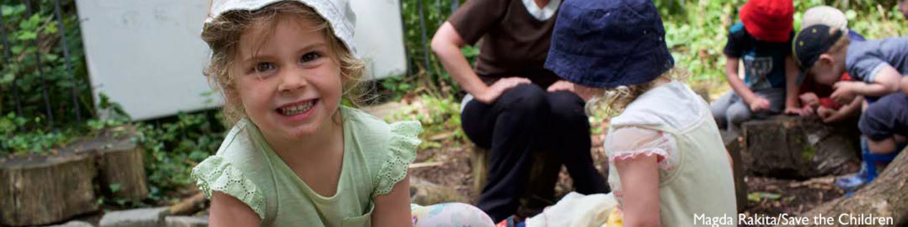 bimba sorridente in primo piano, sullo sfondo altri bambini e bambine che giocano insieme