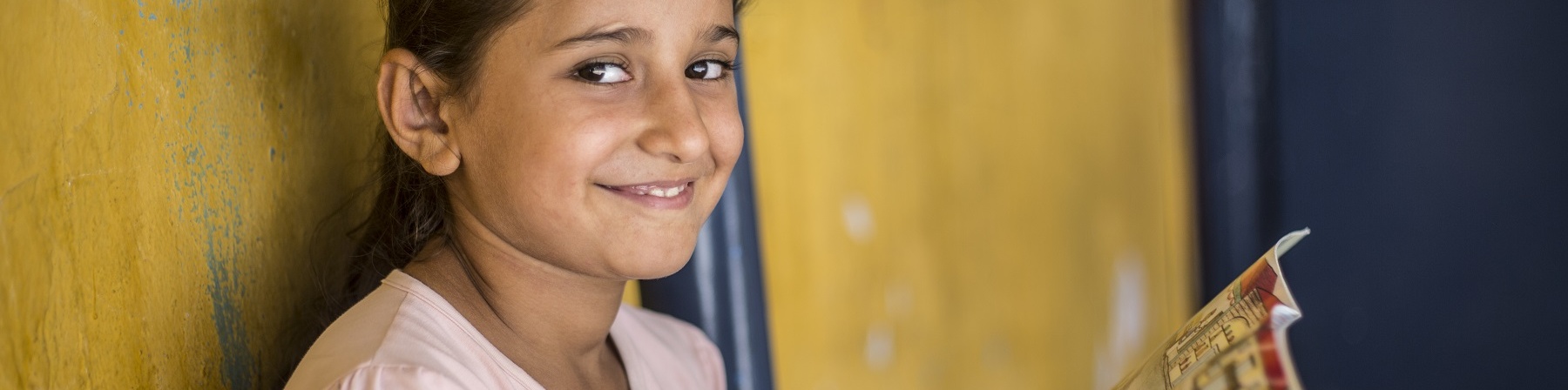 Bambina sorridente guarda in camera mentre tiene in mano un libro aperto e colorato