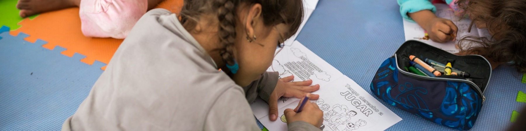 bambina sdraiata per terra su un tappeto colorato disegna