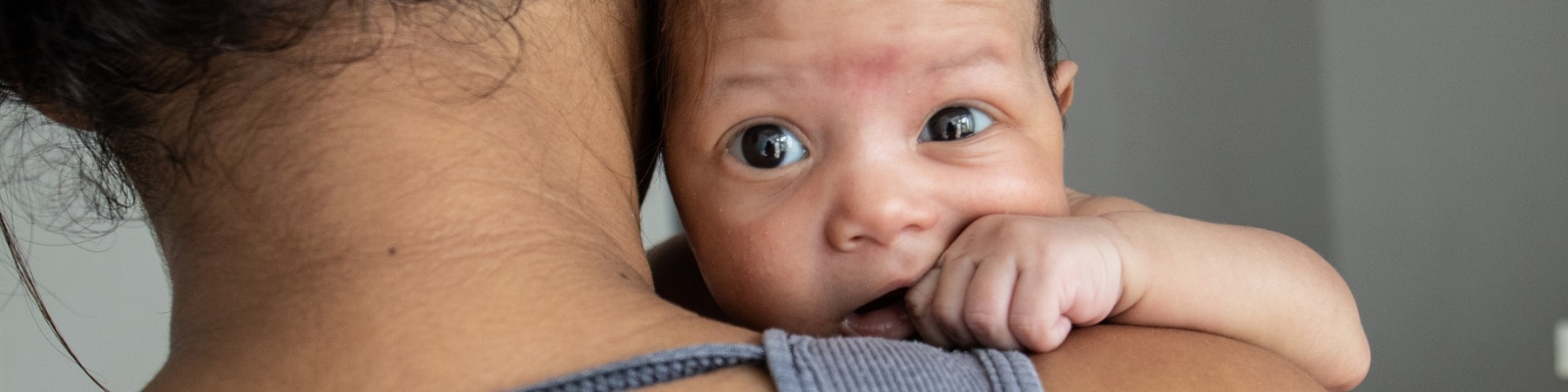 mamma di spalle con in braccio il suo neonato che guarda in camera