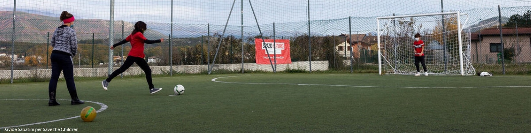 campo da calcio in cui giocano 3 bambini e una di loro si appresta a tirare in porta