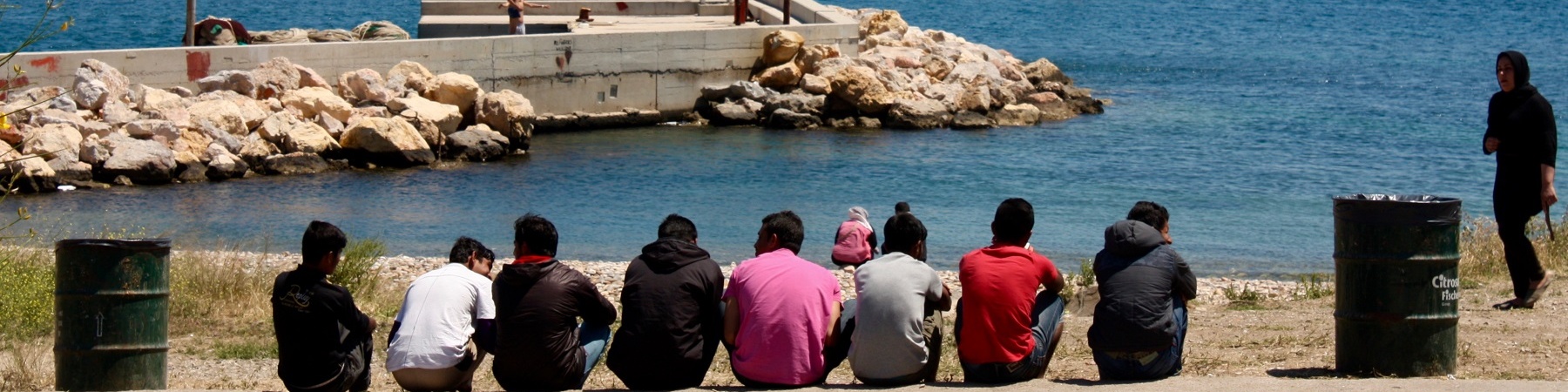 bambini migranti di spalle seduti davanti al mare