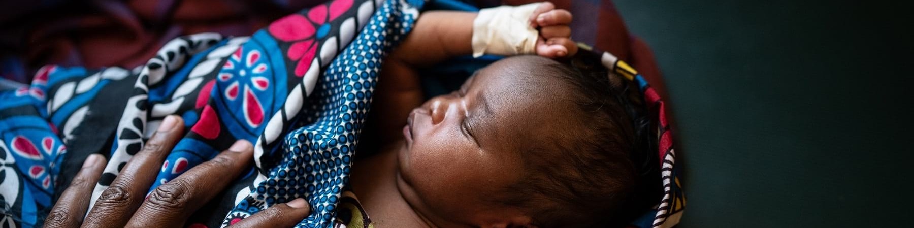 Neonato con manina fasciata avvolto in un telo multicolore