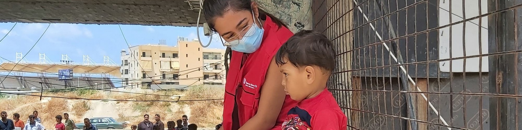 Operatrice Save the Children seduta su un muretto insieme a un bambino accanto a lei