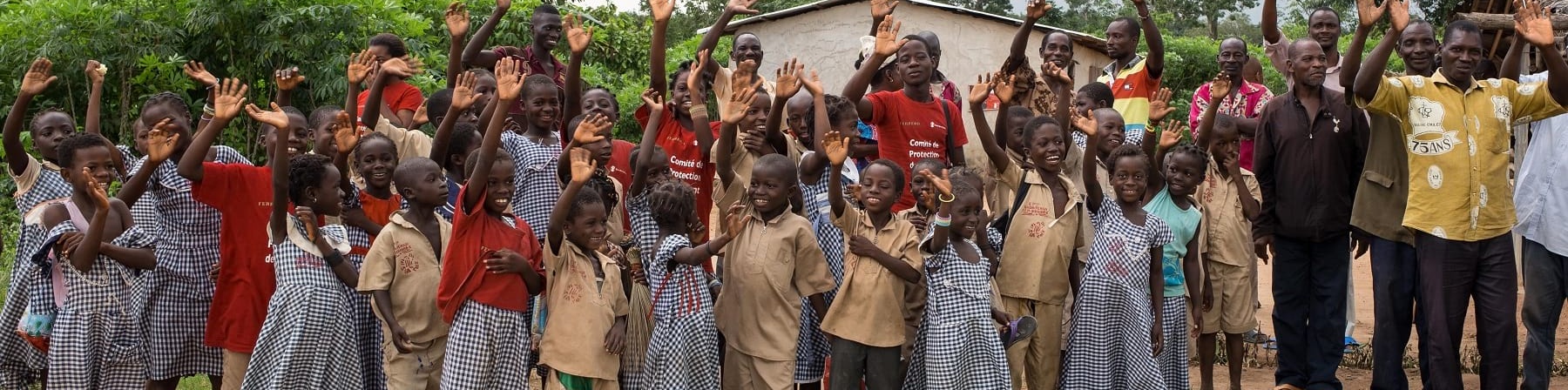 Comunita del cacao Ivoriana di bambini e adulti posa per una foto di gruppo davanti ad alcune case del villaggio