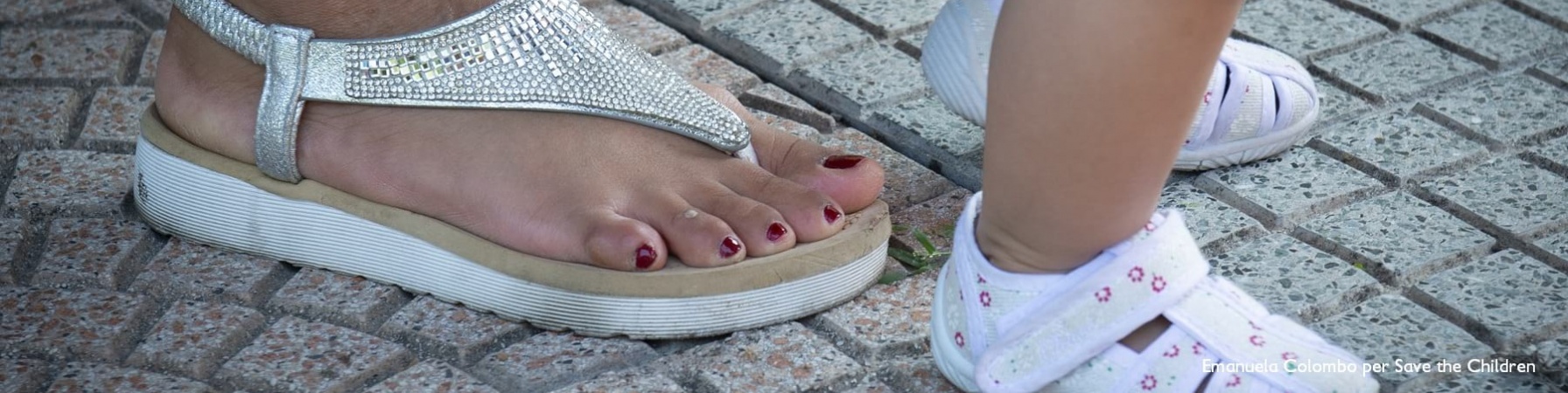 4 piedi, due di una donna con i sandali e due di un bambino piccolo sono posizionati uno davanti all altra