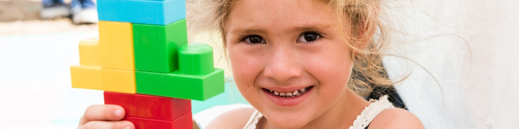 bambina sorridente con in mano una costruzione fatta di Lego colorati