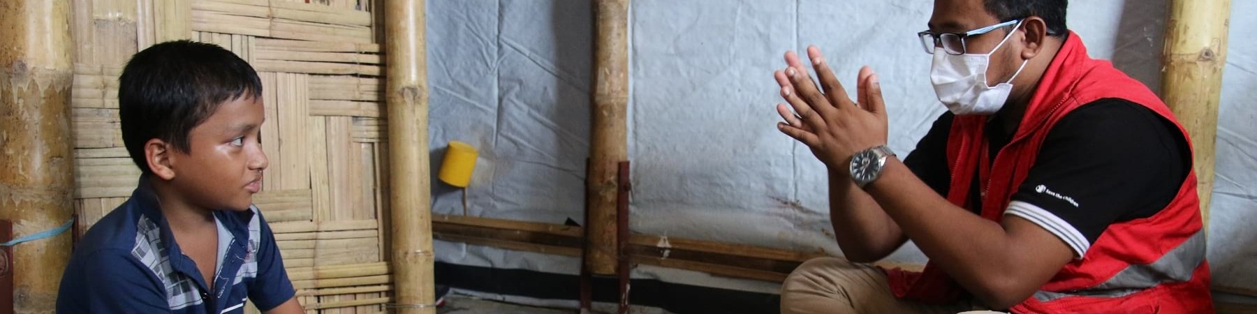 un operatore Save the Children seduto a terra parla con un bambino seduto a terra di fronte a lui