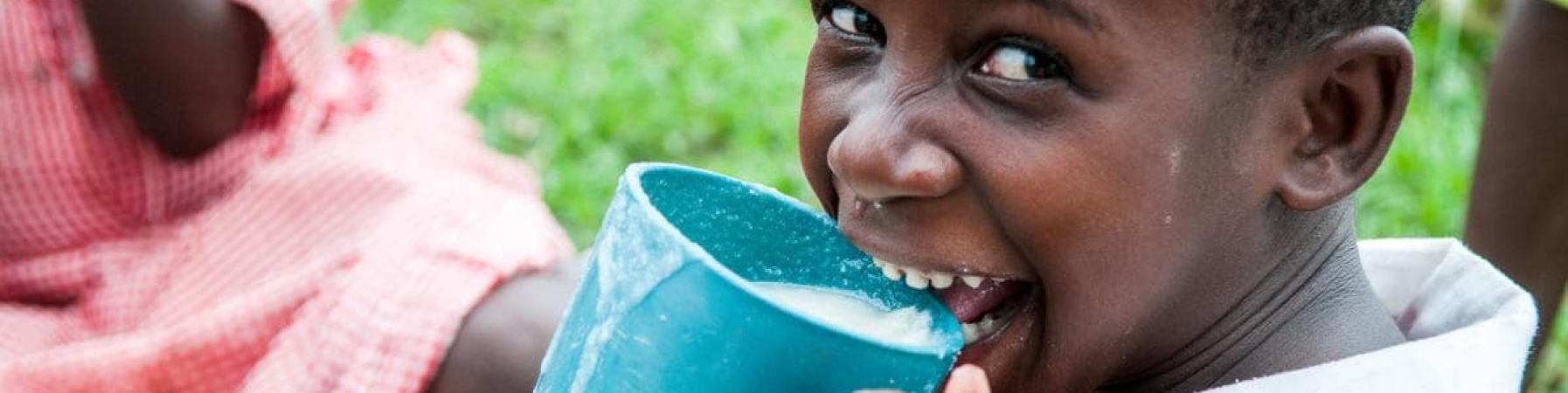 bambina che ride mentre beve da un bicchiere azzurro il latte donato tramite le donazioni 