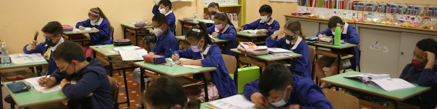 bambine e bambini sui banchi di scuola che scrivono su un foglio 