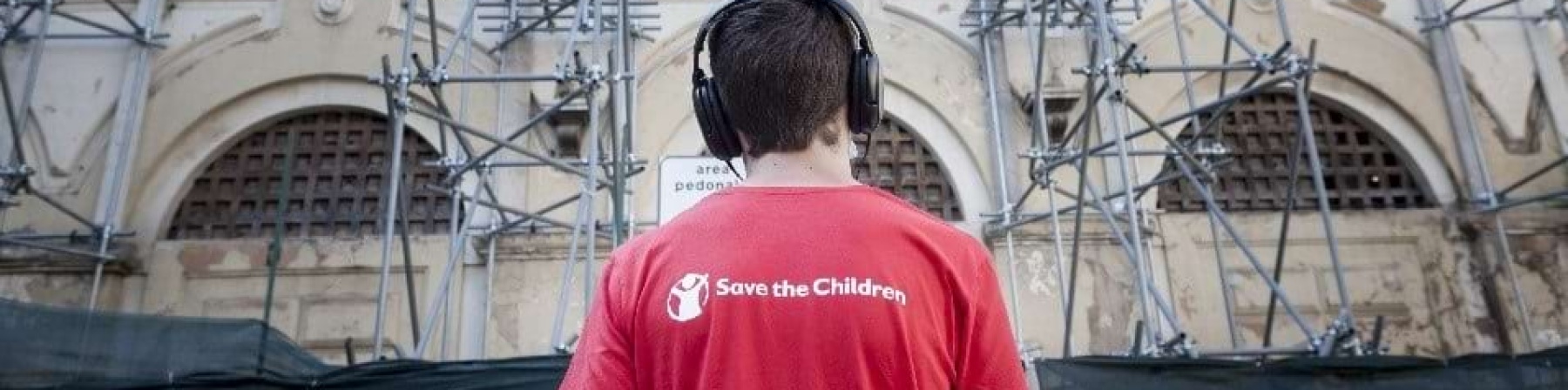 Ragazzo di spalle indossa maglietta Save the Children e cuffie alle orecchie