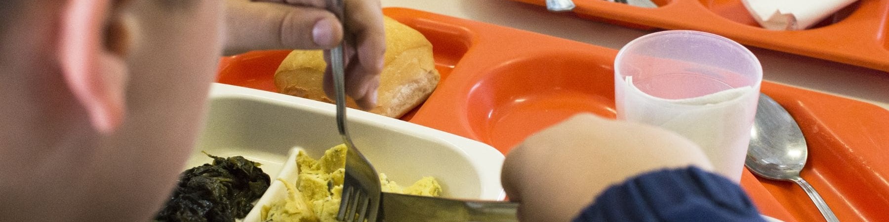 bambino di spalle che mangia in una mensa scolastica