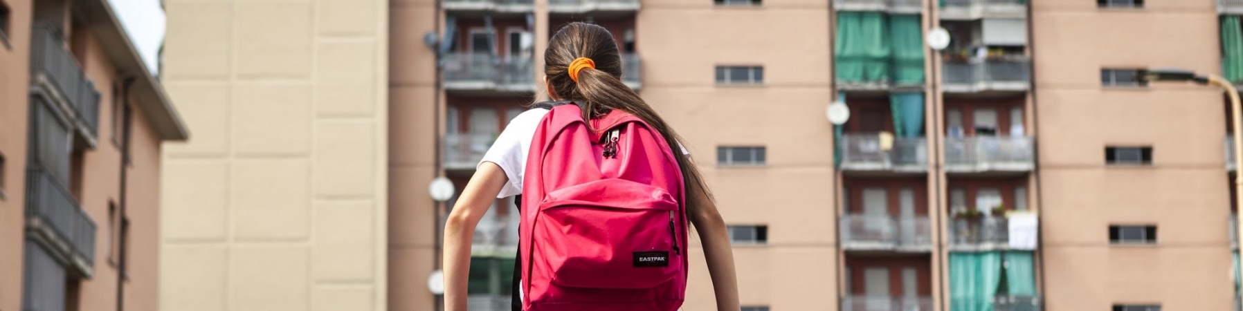 bambina seduta su una ringhiera verde davanti a dei palazzi