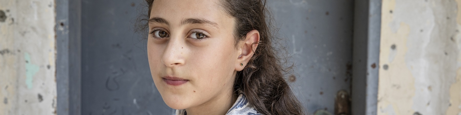 Mezzo busto di una bambina palestinese con fiocco bianco in testa e camicetta maniche corte bianca.