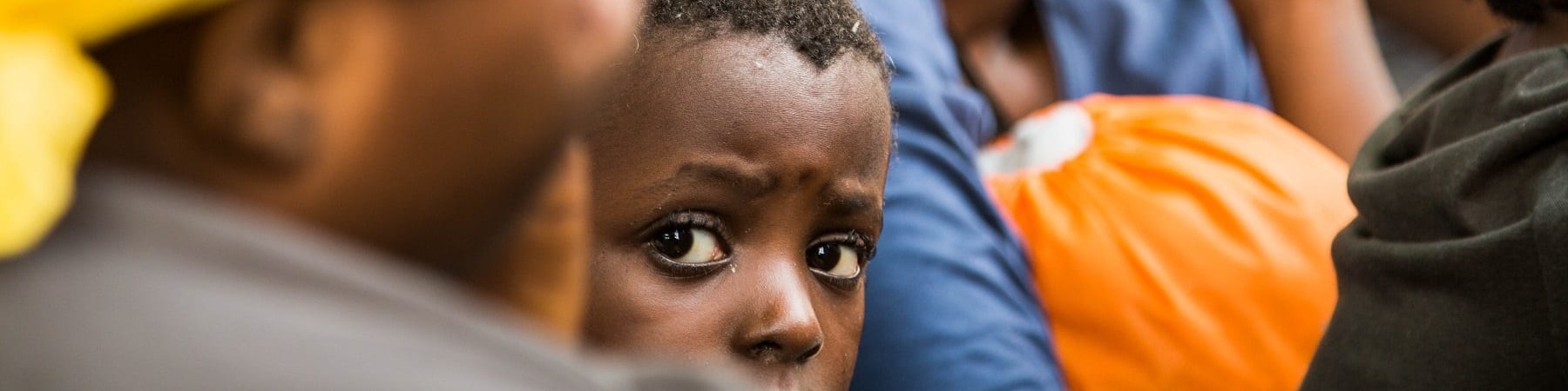 Spunta la testa di un bambino tra i corpi di spalle di alcune donne che sitrovano vicino a lui e che risultano sfocate nell immagine