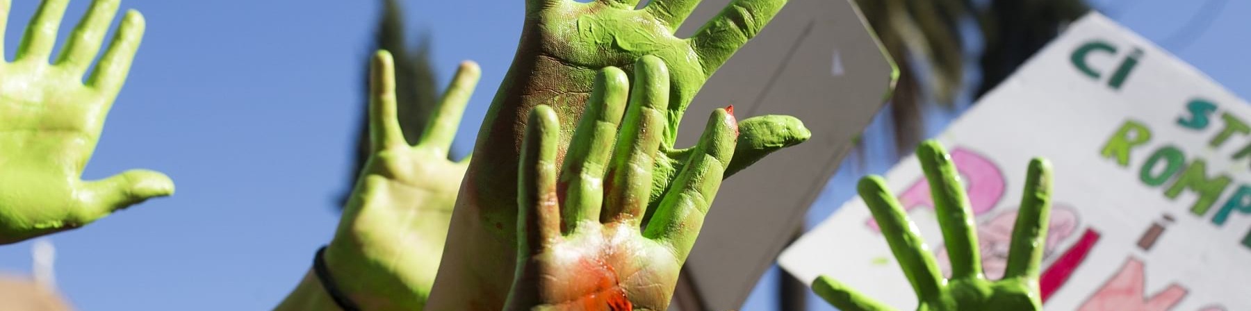 Mani verdi di bambini alzate al cielo con cartelloni