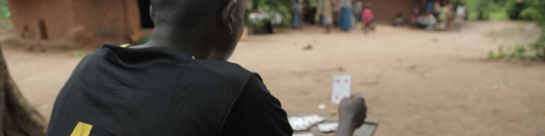 un ragazzo congolese seduto di spalle gioca a carte