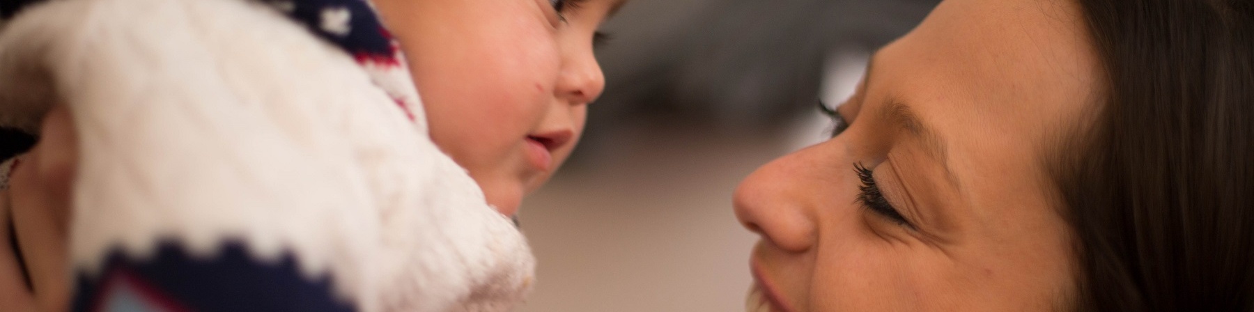 Primo piano di donna che guarda la bimba sollevata in braccio davanti lei.