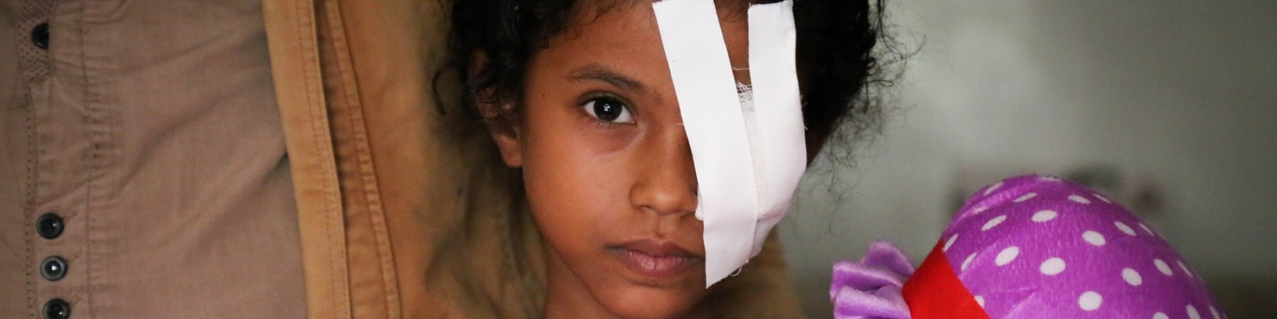Bambina yemenita con bende sull'occhio sinistro abbraccia la sua bambola