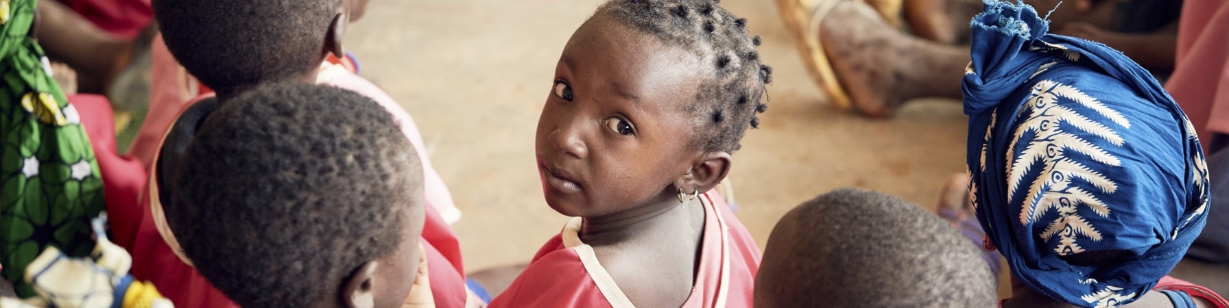 Bambini maliani in cerchio di spalle e al centro una bambina girata guarda in camera