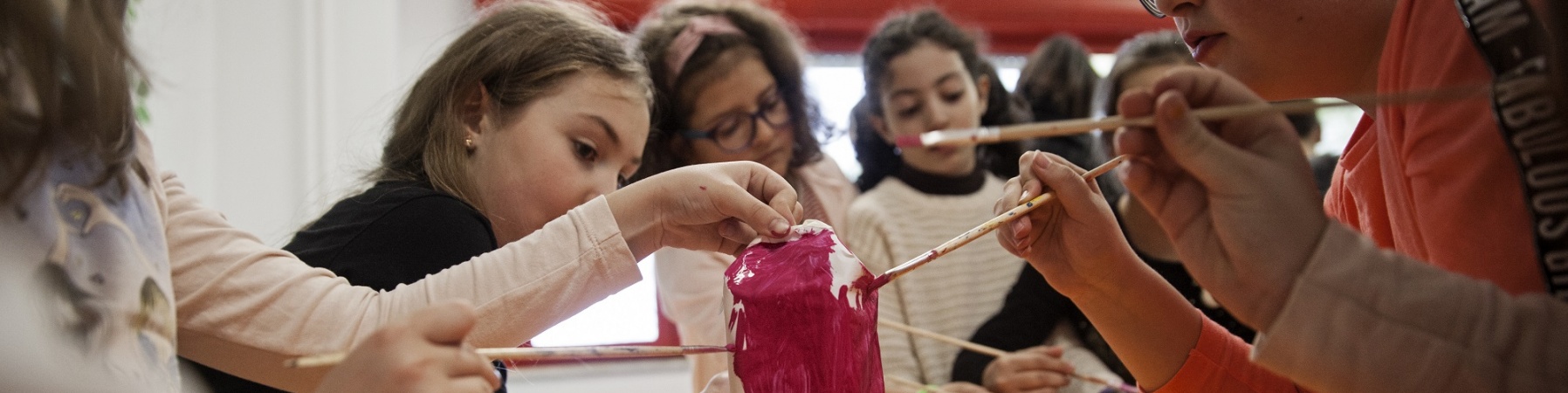 5 ragazze al banco di scuola stanno dipingendo di rosa un loro lavoro artistico